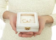 a person holding a small white box with a gold ring in it's hand