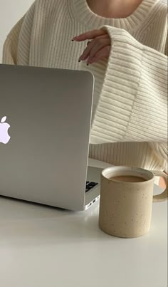 a woman sitting at a table with an apple laptop in front of her and a cup of coffee next to her