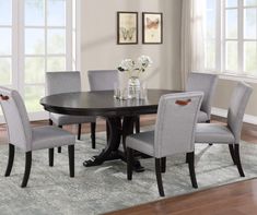 a dining room table with grey chairs and white flowers in vases on the rug