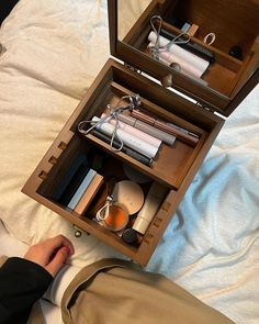 a person is sitting on a bed with their feet propped up next to an open wooden box