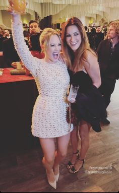 two beautiful young women standing next to each other in front of a table full of people