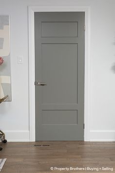 an empty room with a gray door and white walls in front of a painting on the wall