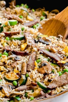 a pan filled with rice and vegetables next to a wooden spoon