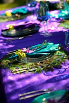 a purple table cloth with peacock feathers on it and place settings in front of them