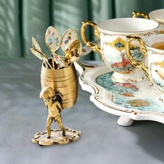 a tea cup and saucer with some gold decorations on it, next to a figurine