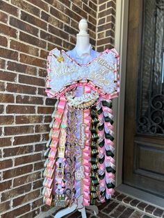 a dress made out of ribbons on a mannequin stand in front of a brick wall