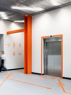 an orange and white entrance to a building with two people walking by in the background