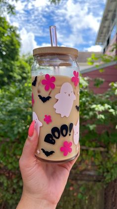 a hand holding up a glass jar with some stickers on it and trees in the background