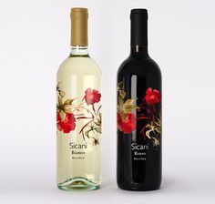 two bottles of wine sitting next to each other on a white surface with flowers painted on them