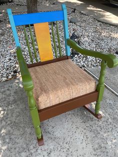 a wooden rocking chair sitting on top of a gravel covered ground next to a tree