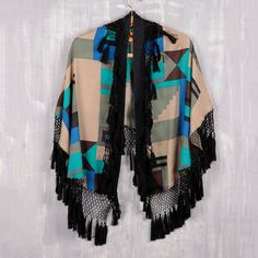 Cloak yourself in warmth and style wearing this bold wrap from India's Arnab Roy. Crafted from 100% wool, the wrap features a vivid geometric design screen printed in hues of ultramarine, turquoise, and beige. A black cotton macrame trim adorned with black tassels adds a playful yet elegant touch. Wool Wrap, Black Fringe, Cloak, Geometric Design, Black Cotton, Macrame, Tassels, Kimono Top, Turquoise