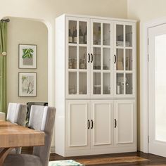 a white china cabinet with glass doors in a dining room area next to a wooden table