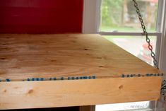 a wooden shelf with chains hanging from it's sides in front of a window