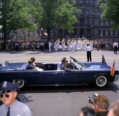 an old car driving down the street with people in uniform onlookers watching