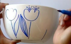 two hands holding a white bowl with blue designs on it and one hand is writing