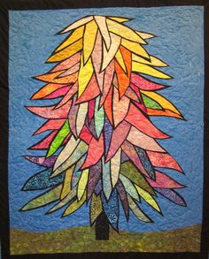 a colorful tree made out of many different colored leaves on a blue quilted wall hanging