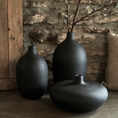 two black vases sitting next to each other on a table with a stone wall behind them