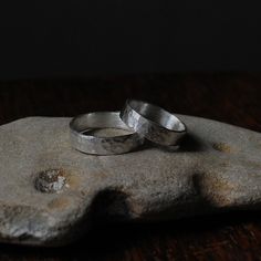 two silver wedding rings sitting on top of a rock in front of a black background