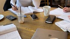 three people sitting at a table with papers and laptops on it, one holding a pen