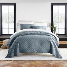 a bed with blue comforter and pillows in a room next to two large windows