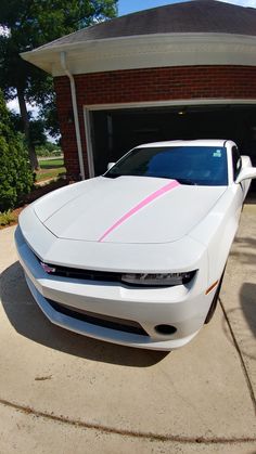 a white sports car parked in front of a garage with pink stripes on the hood