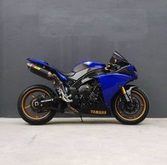 a blue and black motorcycle parked in front of a gray wall with gold rims