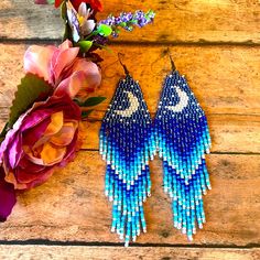 two pairs of blue and white beaded earrings next to a bouquet of flowers on a wooden surface