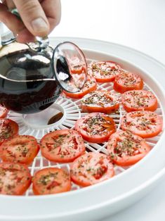 a person pouring sauce on tomatoes in a white tray with other food items around it