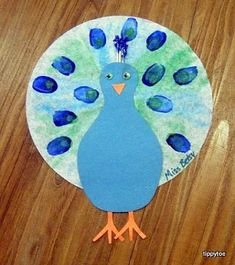 a paper plate with a blue and green peacock painted on it's side, sitting on a wooden surface