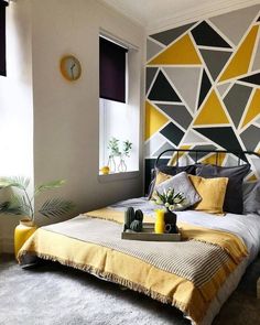 a bed with yellow and gray sheets in a bedroom next to a clock on the wall