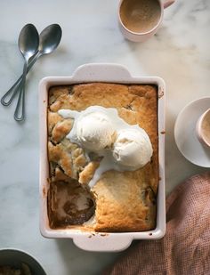 a dessert with ice cream on top in a dish next to two cups and spoons