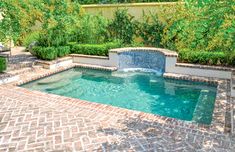 a small pool surrounded by brick pavers and shrubbery, with a fountain in the middle