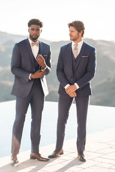 two men in suits standing next to each other on a ledge looking at the camera