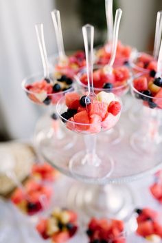 desserts are arranged in small bowls on a cake stand with strawberries, blueberries and watermelon