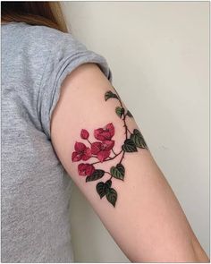 a woman's arm with red flowers and green leaves on the left side of her arm