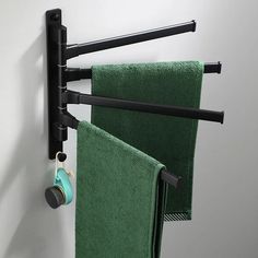 two green towels hanging on the wall next to a towel rack with black metal bars