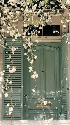 an open green door with white flowers growing on the outside and side of it, in front of a building