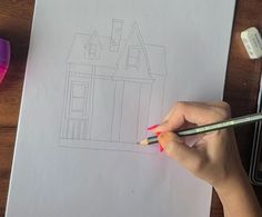 a person is drawing a house with colored pencils