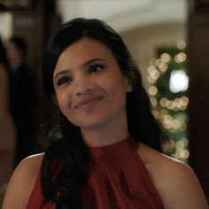 a woman in a red dress smiles at the camera while standing next to a christmas tree