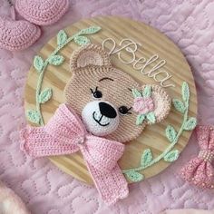 a crocheted teddy bear with a pink bow laying on top of a wooden plate