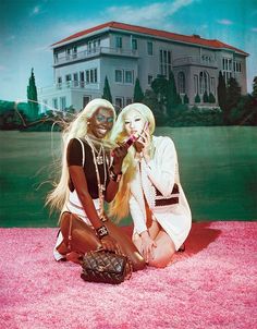 two beautiful women sitting on the ground in front of a large white house with pink carpet