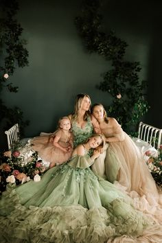 three women in dresses sitting on a bed with flowers and greenery around them, posing for the camera