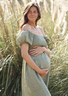 a pregnant woman in a green dress poses for a photo with tall grass behind her