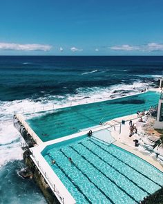 an outdoor swimming pool next to the ocean with swimmers in it and onlookers