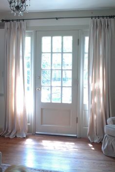 an empty living room with white furniture and curtains on the windowsill, in front of a french door