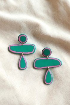 two pairs of pink and green earrings sitting on top of a white sheet