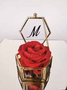 a red rose in a gold box with the letter m on it's side