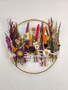 an arrangement of wildflowers and grasses arranged in a circle on a white wall