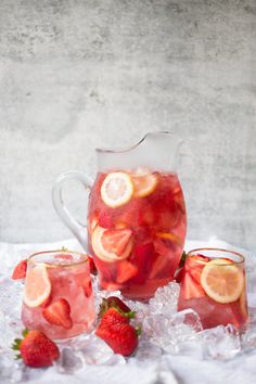 a pitcher and two glasses filled with water, lemons and strawberries on ice