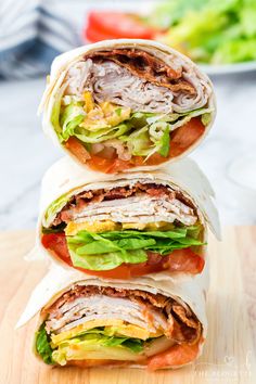 three wraps stacked on top of each other with lettuce and tomatoes in the background